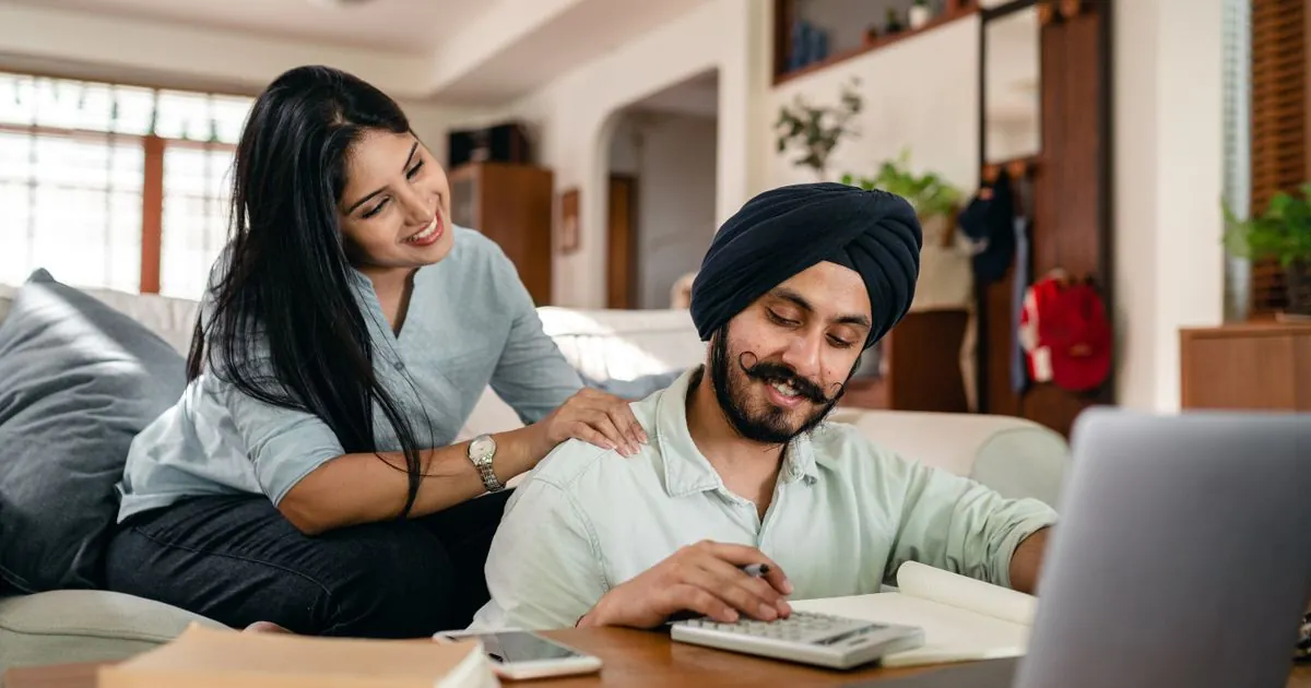 Couple working out 1000 loan Canada repayment numbers with a calculator and laptop at home