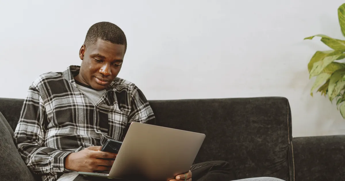 Man on his sofa comparing $2000 loan offers on a laptop and phone at home in Canada