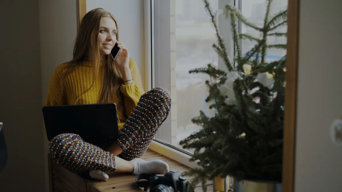 Young woman on the phone to her lender asking for a cosigner release, laptop on her knees