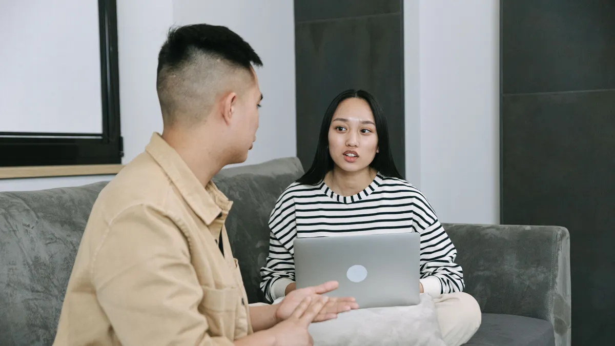 Two friends on a sofa working out what a loan with a cosigner would save, laptop open