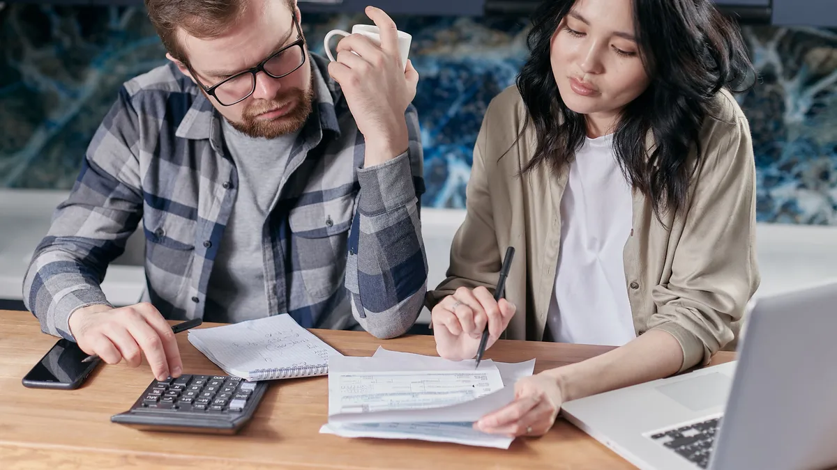 Couple working out a loan for bad credit payment with a calculator and their monthly bills at the kitchen table